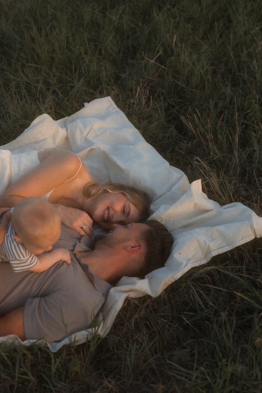 Katharina mit ihrem Mann und Baby auf einer Decke im Gras; vom Baby ist der Hinterkopf zu sehen